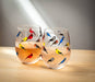 Multi Bird Stemless Wine Glass by Abbott filled with refreshing beverages, featuring whimsical birds in various bright colors on a clear glass surface.