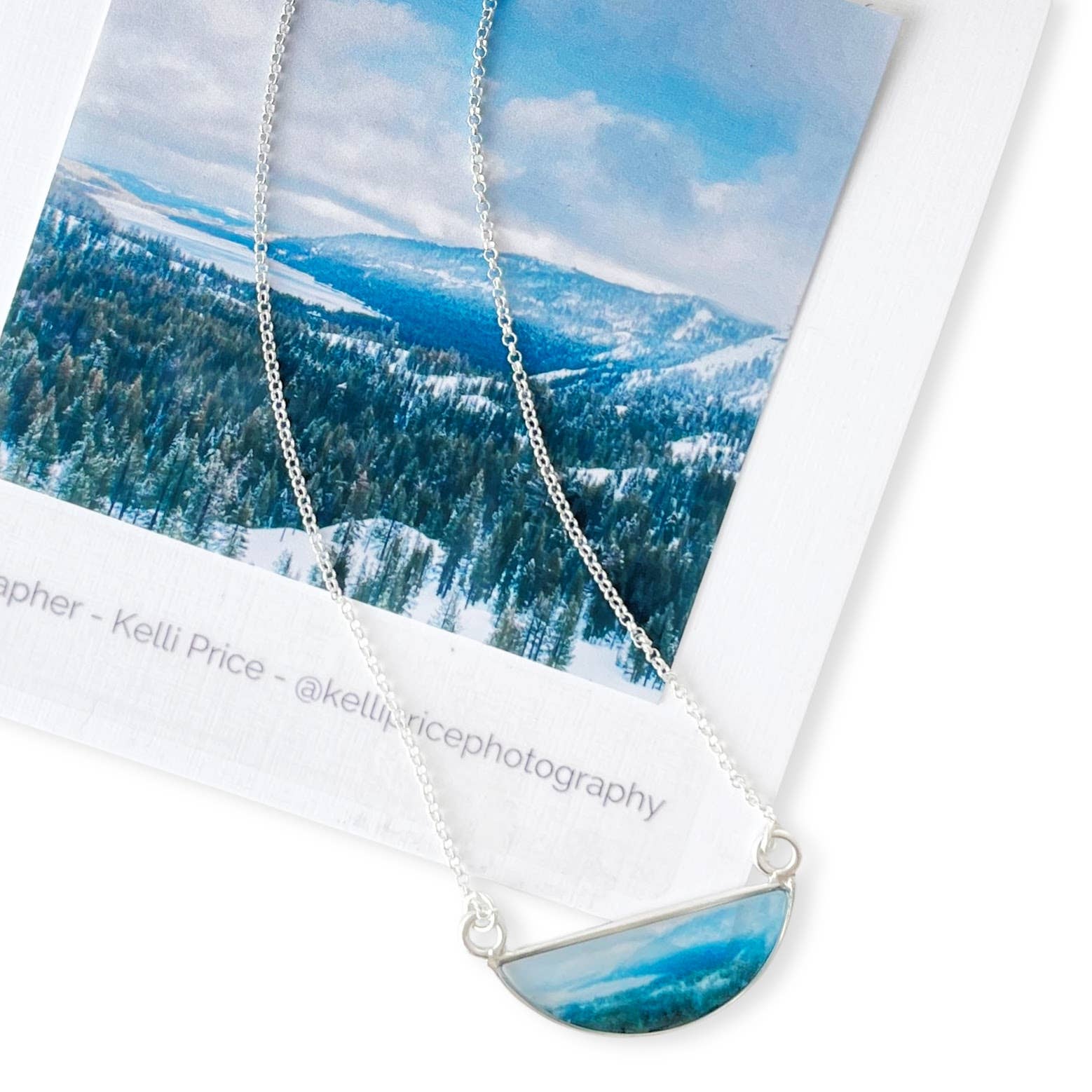 Tahoe Snow Necklace by Foterra Jewelry, showcasing a unique design featuring a scenic image coated in waterproof UV resistant resin, set on an 18-inch sterling silver chain, presented with a beautiful landscape photograph.