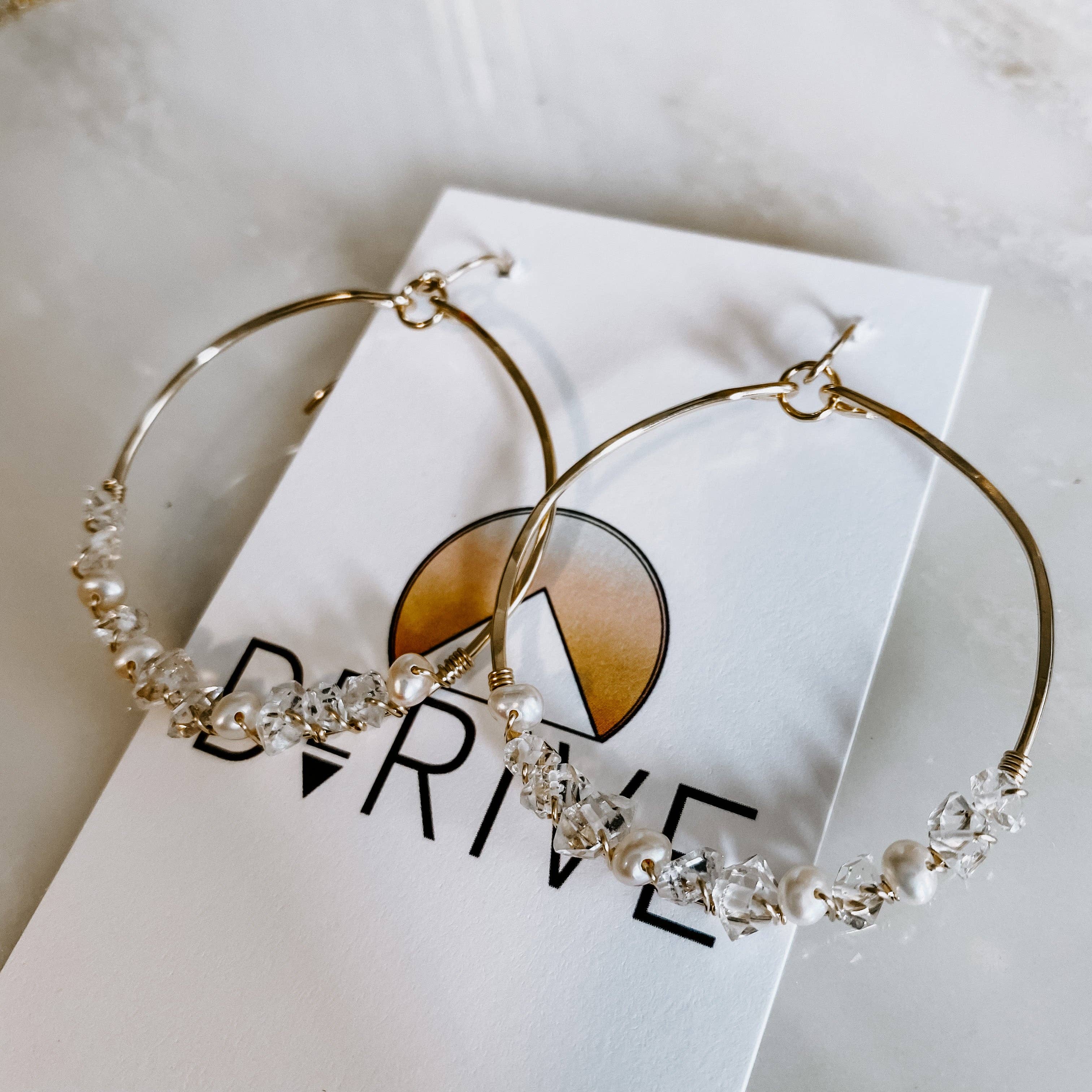 Flat lay of Everly Herkimer Diamond and Pearl Hoop Earrings by Derive Jewelry on branded packaging, featuring exquisite diamonds and pearls on elegant hoops.