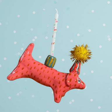 Red ceramic dog-shaped candle holder with a lit candle on a gray background