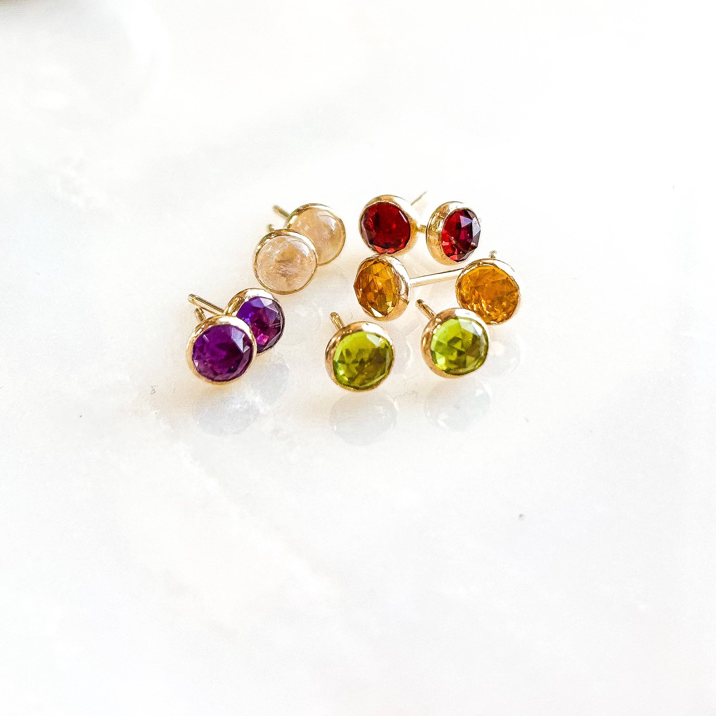 Gemstone Stud Earrings from Derive Jewelry featuring a selection of colorful gemstones in gold fill settings, arranged beautifully on a marble surface.