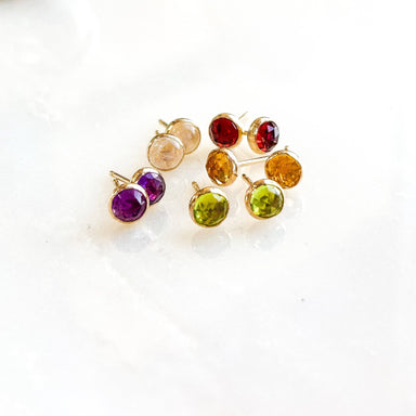 Gemstone Stud Earrings from Derive Jewelry featuring a selection of colorful gemstones in gold fill settings, arranged beautifully on a marble surface.