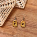 Olive Square Loop Ceramic Stoneware Earrings by The Artifact House resting on a woven surface, highlighting their handmade elegance.