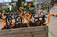 A wooden planter box filled with multiple curled, snake-like sculptures in glossy black and bright orange, photographed outdoors with a blurred garden or market background.