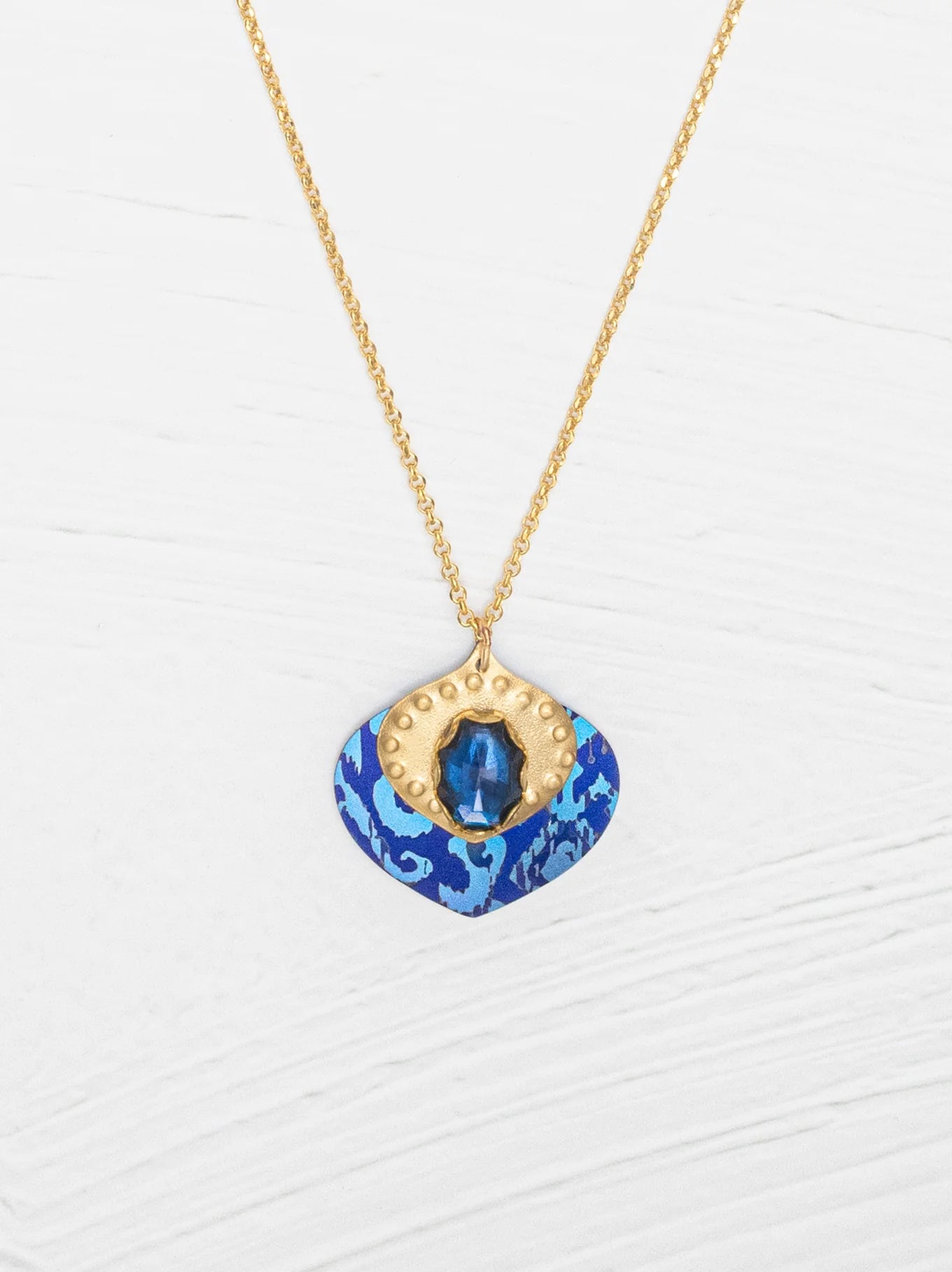 Arabella Pendant Necklace featuring a vibrant glass stone and textured gold on a glowing niobium backdrop.